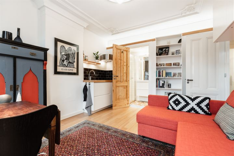 Overzicht van de studio. De studio wordt gestoffeerd en gedeeltelijk gemeubileerd opgeleverd. De bedbank op deze foto staat er en een tafeltje. Er zijn zware, rood fluwelen gordijnen.